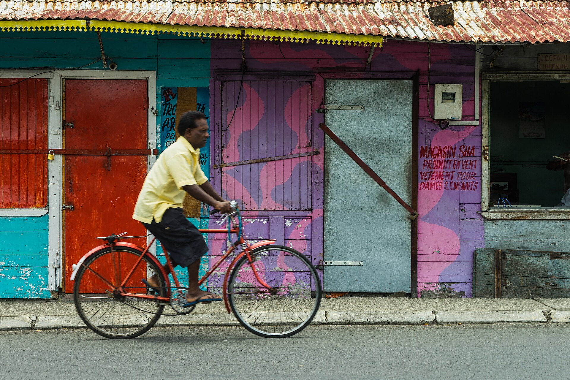 A cyclist passing painted shopfronts in Mahébourg